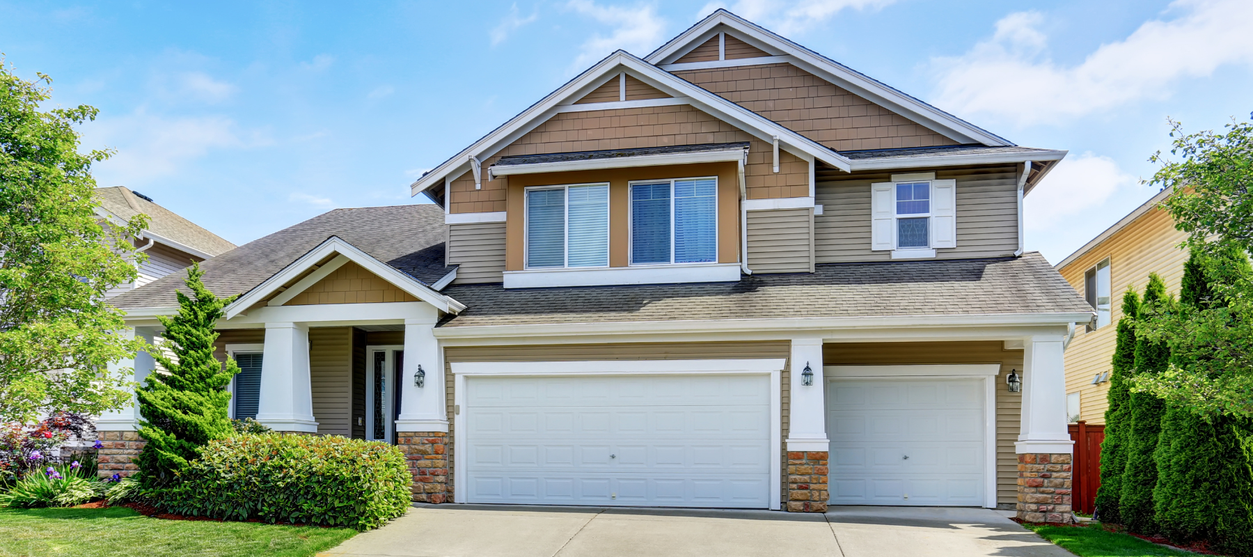 The curbside of a beige home with a two car garage on a clear day